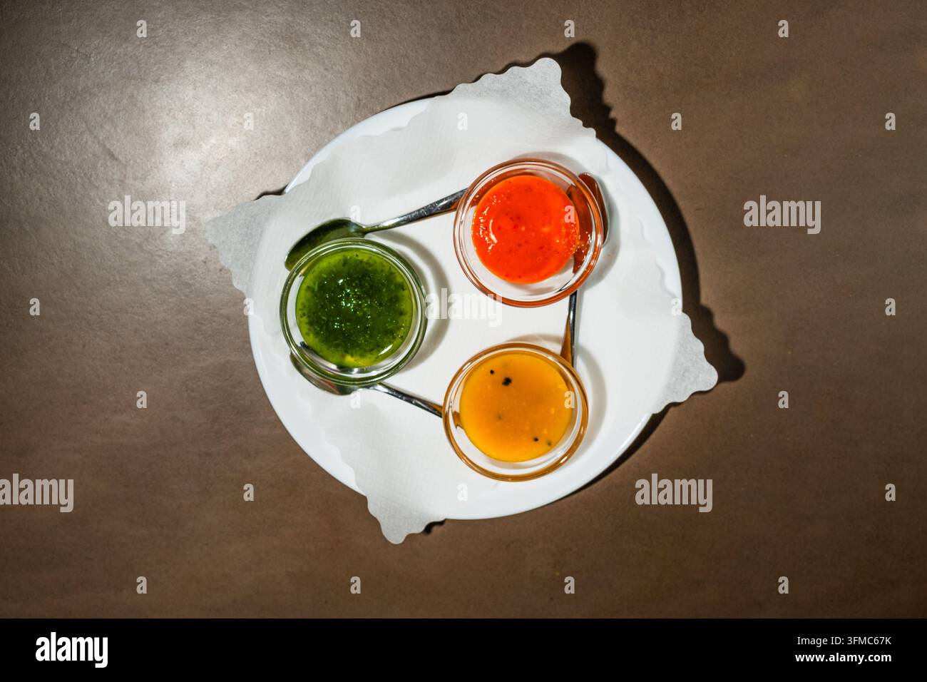 Drei indische Chutneys, Minze, Mango und Tamarinde, in kleinen Schüsseln auf einem weißen Teller, Ansicht von oben Stockfoto