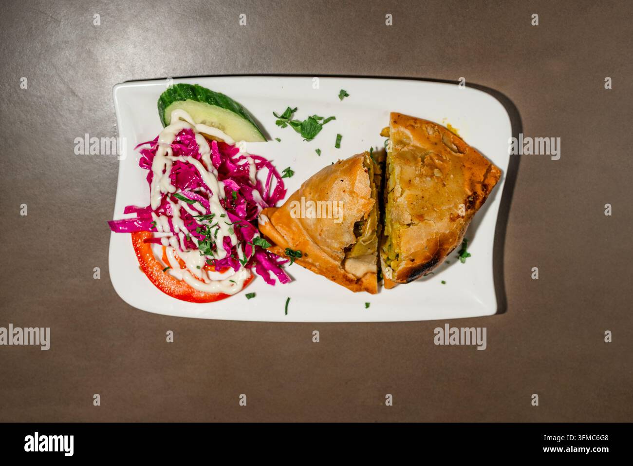 Gemüse-Samosa mit Rotkohl-Salat und Limette auf einem weißen Teller, Ansicht von oben Stockfoto