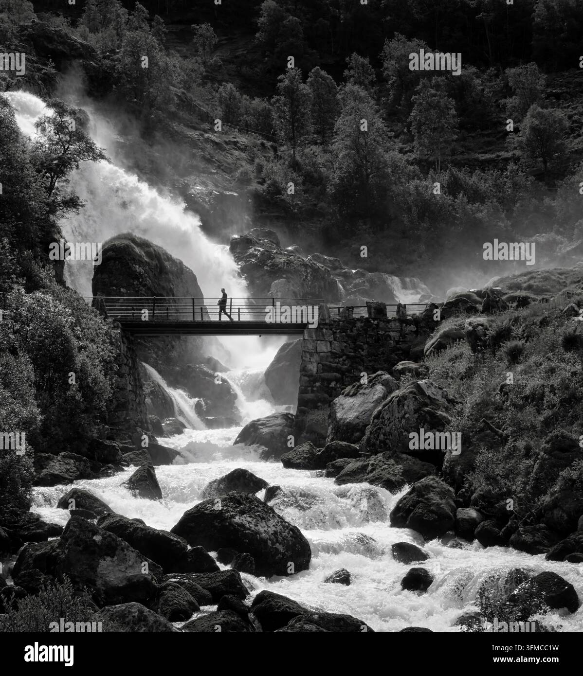 Mutig den Sprühregen des Kleivafossen ertragen, während das Schmelzwasser des Briksdalsbreen-Gletschers diejenigen erwischt, die die Fußbrücke überqueren. Stockfoto