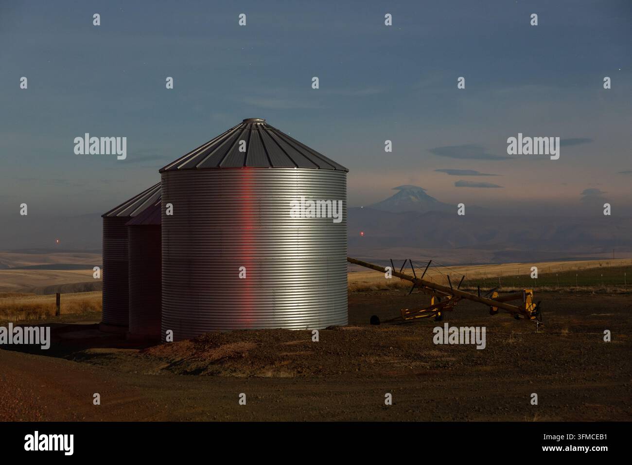 Getreidesilos auf Ackerland mit einem Berg in der Dämmerung Stockfoto