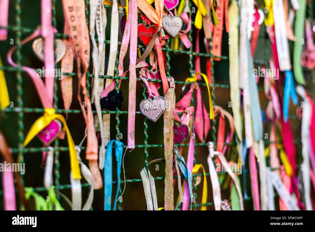 Bunte Wunschbänder mit Herz-Anhängern, die an einem Zaun befestigt sind Stockfoto