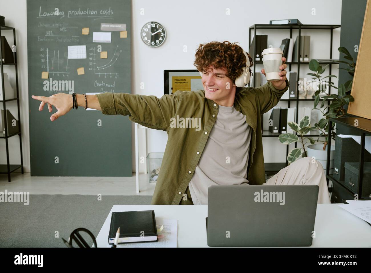 Fröhlicher Mann, der Musik hört und am Bürotisch tanzt Stockfoto