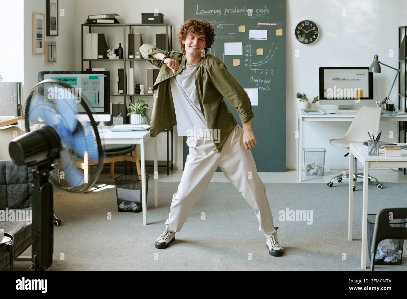 Fröhlicher Mann tanzt vor einem Ventilator in einem modernen Büro Stockfoto