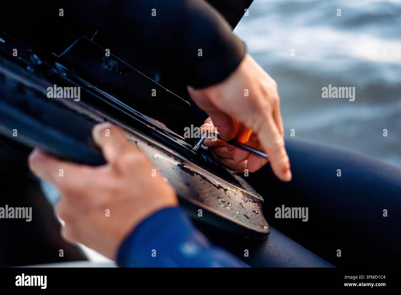 Nahaufnahme von Händen, die einen Inbusschlüssel verwenden, um ein Hydrofoil-Brett in der Nähe des Wassers zusammenzubauen. Stockfoto