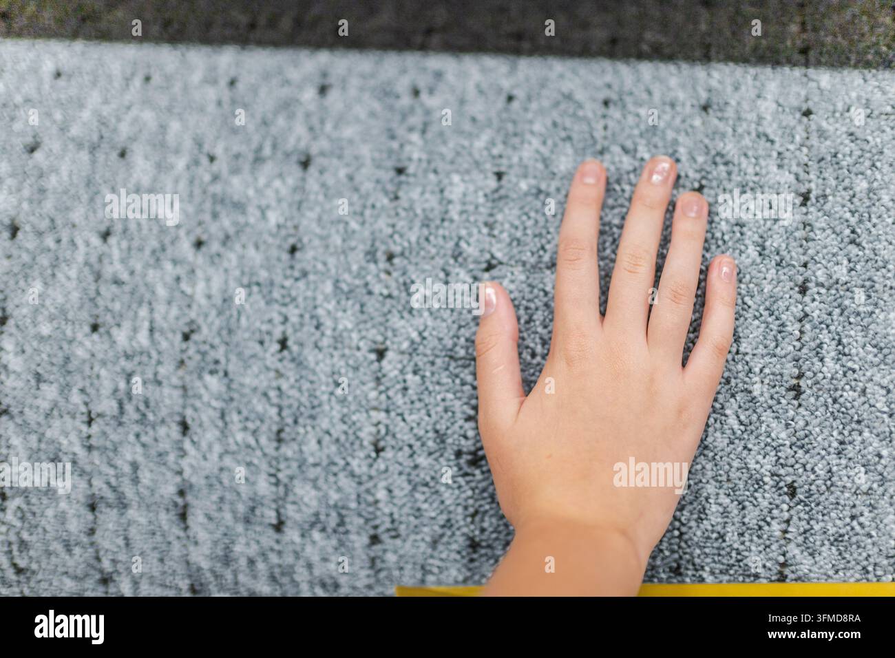 Eine Hand berührt die weiche, strukturierte Oberfläche eines grauen Teppichs. Stockfoto