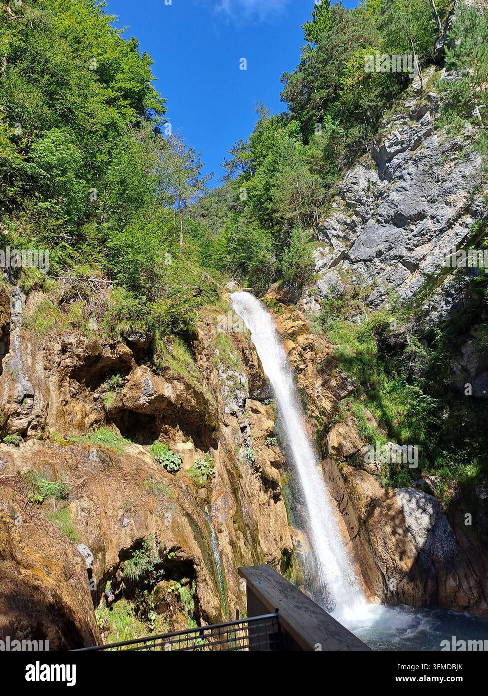 Wasserfall stürzt durch bewaldeten Kalkstein-Canyon unter blauem Himmel - Smartphone-aufgenommenes Stockfoto