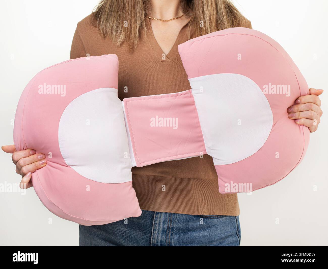 Frau demonstriert rosa Schwangerschaftskissen und hält es in den Händen, Produktfotografie auf hellem Hintergrund Stockfoto