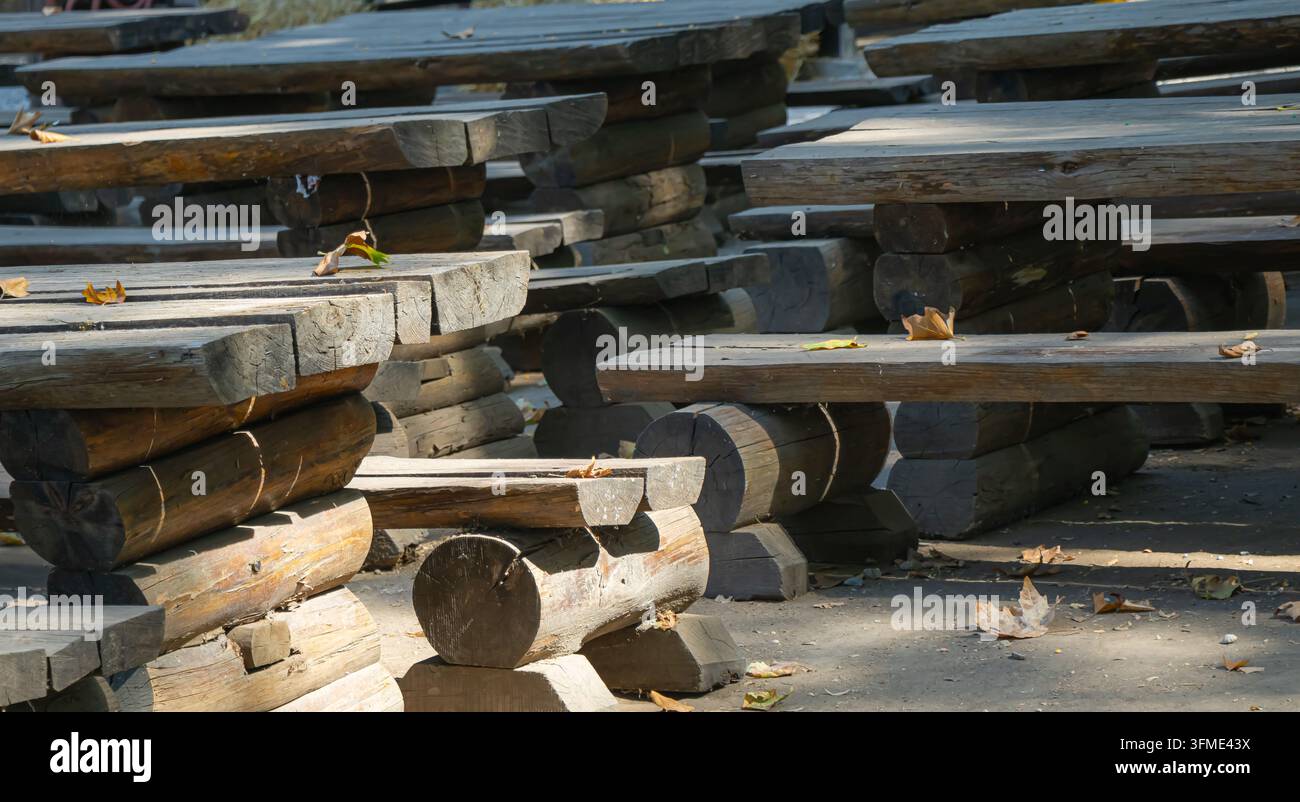 Reihen von schweren rustikalen Holztischen und Bänken aus Baumstämmen und Brettern stehen im Freien zwischen gefallenen Herbstblättern in einem schattigen Erholungsgebiet. Stockfoto