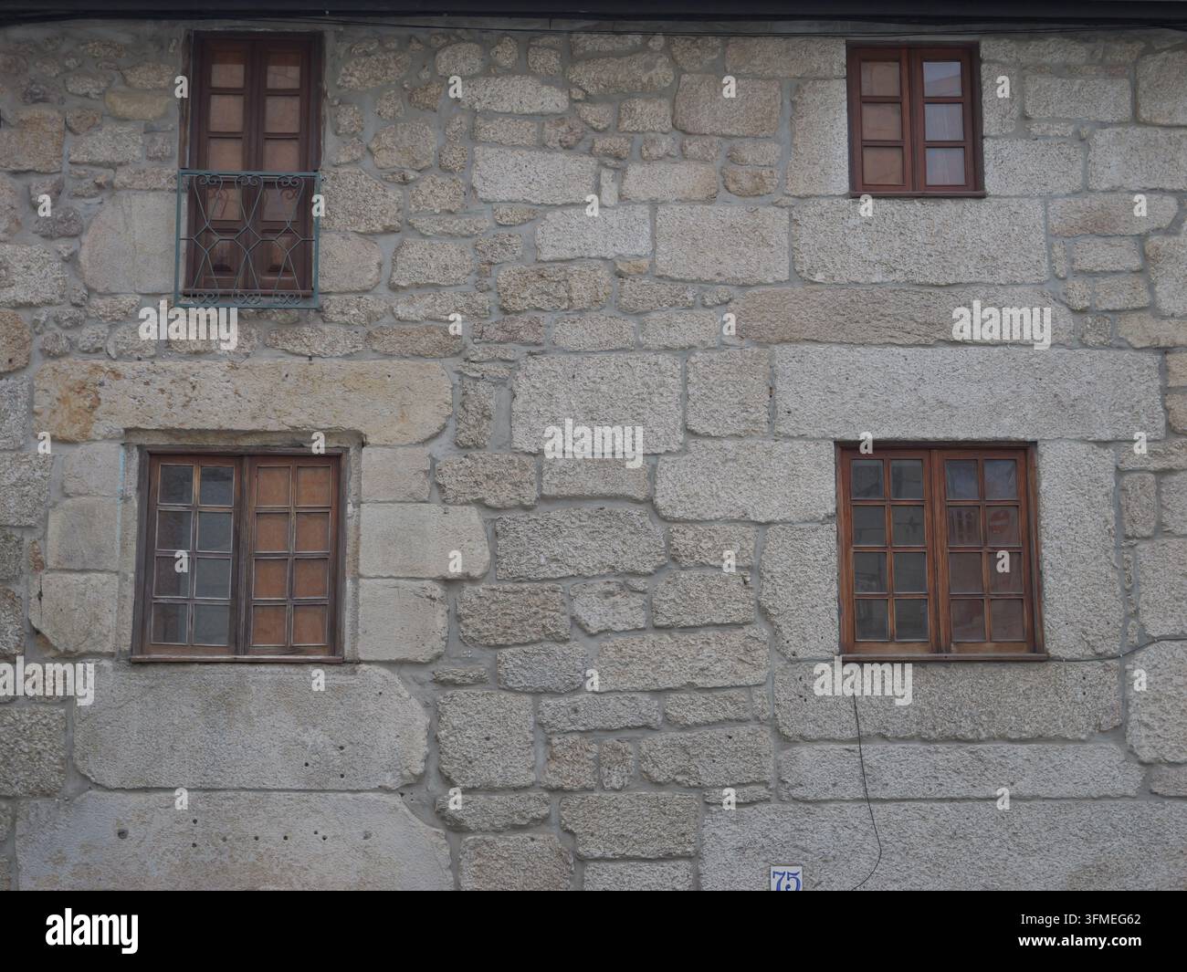 Ansicht einer traditionellen Steinmauer mit drei holzgerahmten Fenstern im historischen Zentrum von Covilha, Bezirk Castelo Branco, Portugal. Stockfoto