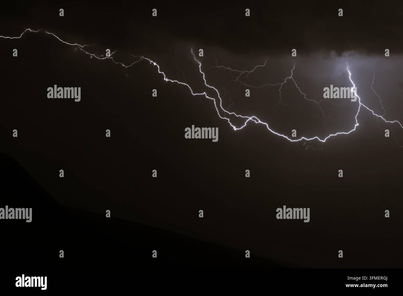Ein mächtiger und verzweigter Blitz erhellt dramatisch den dunklen Himmel während eines Gewitters. Stockfoto