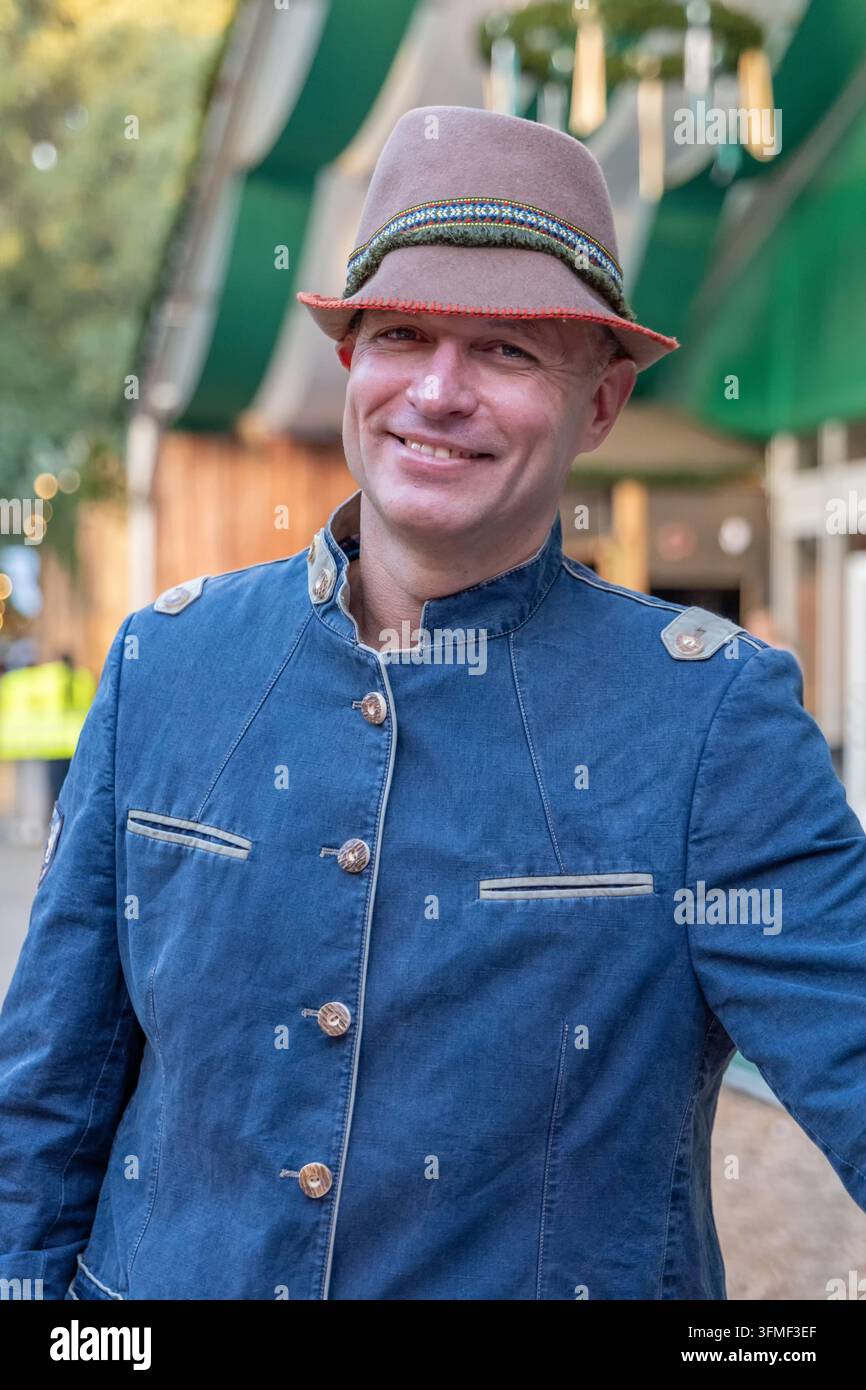 Ein lächelnder Mann trägt einen Hut im bayerischen Stil und eine blaue Trachtenjacke im Freien. Stockfoto