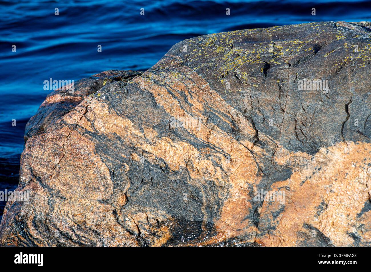 Verwitterter Küstenfelsen mit farbenfrohen Mineralmustern neben tiefblauem Meerwasser. Stockfoto