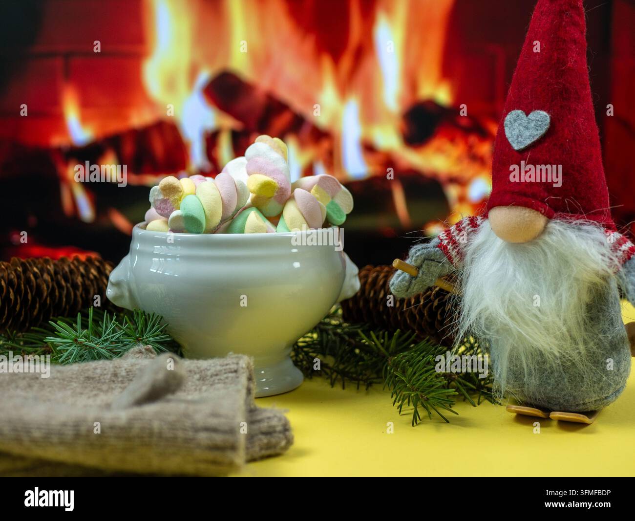 Weihnachts-Neujahrs-Hintergrund mit Marshmallow-Tasse, Zwerg und gestrickter Decke am brennenden Kamin, gemütliche Feiertagsdekoration Stockfoto