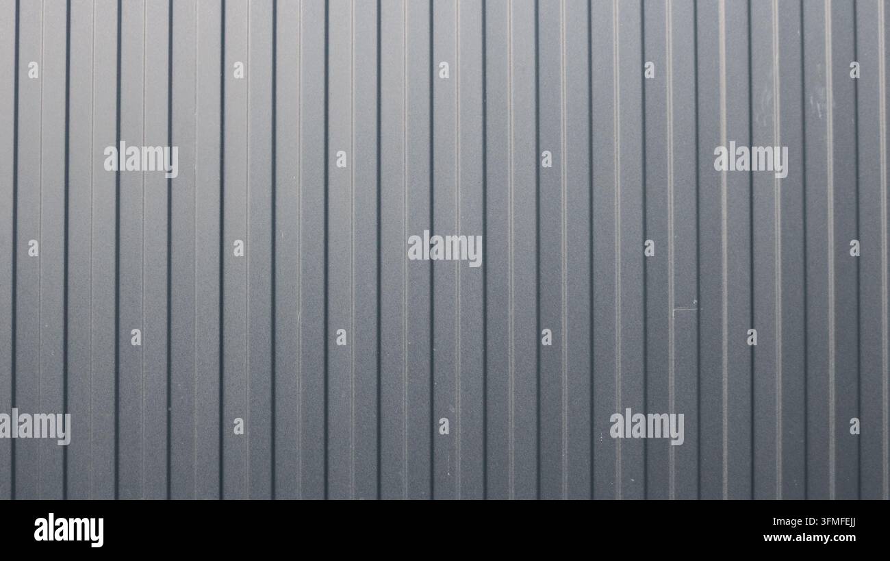 Nahaufnahme der Textur von neuem grauem Wellblech. Eine glatte, matte Oberfläche mit deutlichen vertikalen Rillen und einem gleichmäßigen Graphitton. Stockfoto