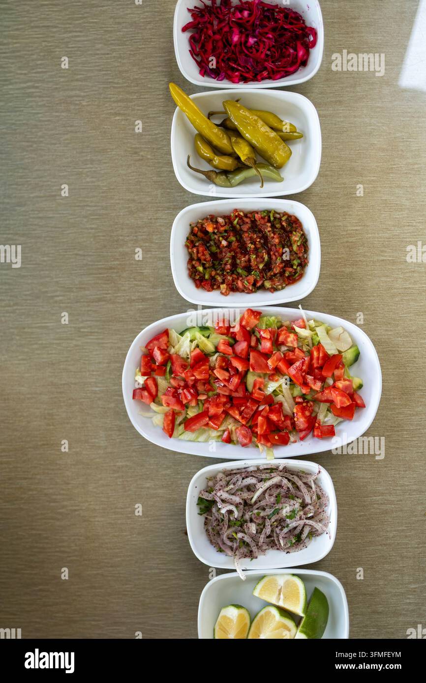 Oberblick über verschiedene türkische Meze, frische Salate, eingelegte Paprika, Zwiebelsalat und Zitronenscheiben, die in weißen Tellern auf einem Restauranttisch angeordnet sind. Stockfoto