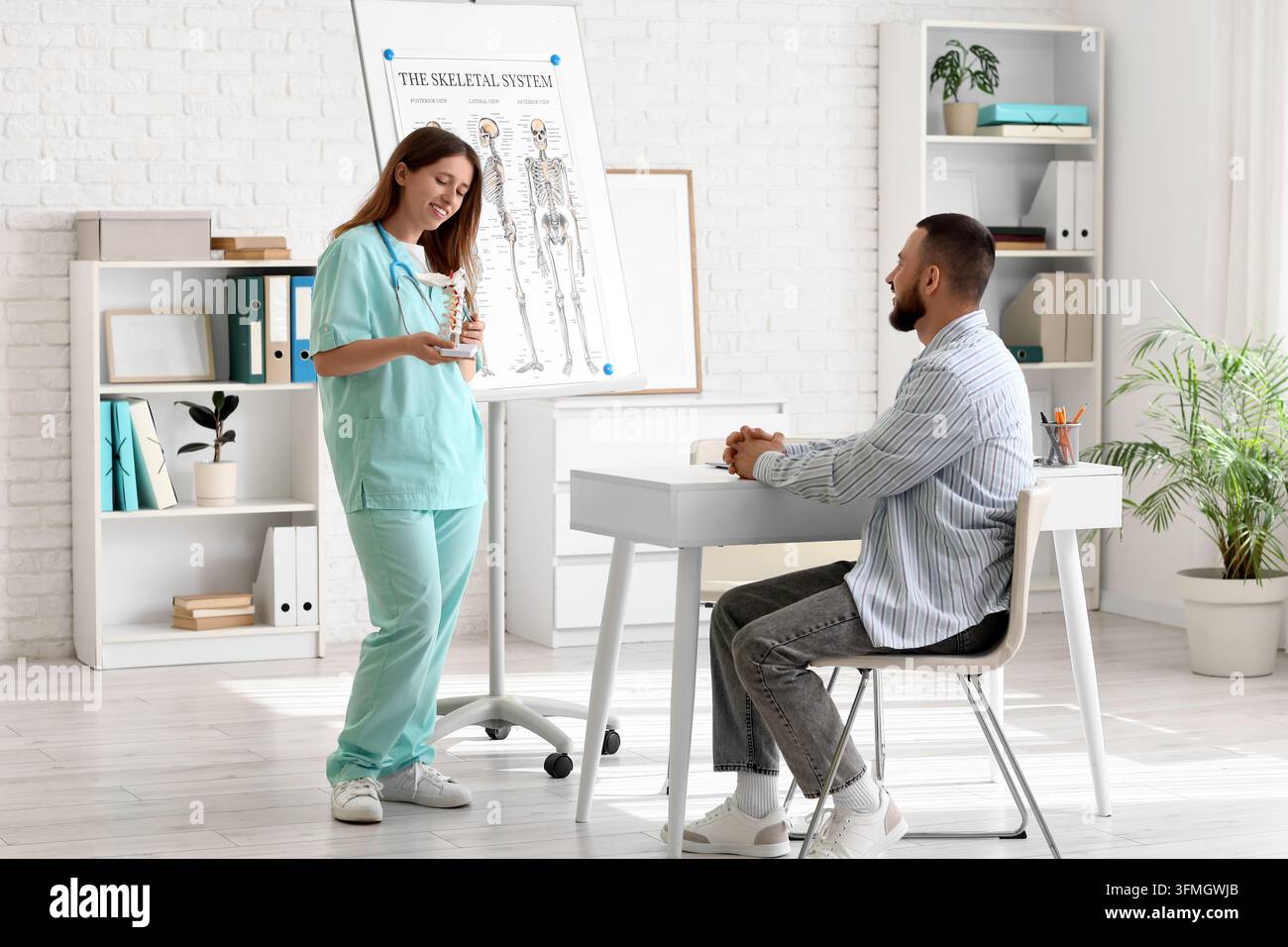 Patientenaufklärung und medizinische Beratung, Arzt erklärt einem männlichen Patienten die Wirbelsäulenanatomie in einer Klinik mit einer Skelettsystemtafel Stockfoto