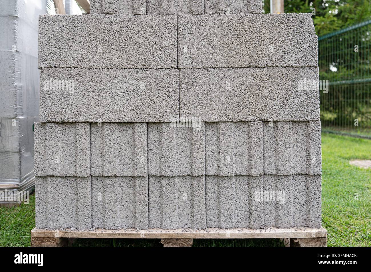 Ein Stapel grauer Betonblöcke, ordentlich auf einer Holzpalette auf einer Baustelle angeordnet. Diese haltbaren Mauerwerksmaterialien sind bereit für den Mauerbau Stockfoto