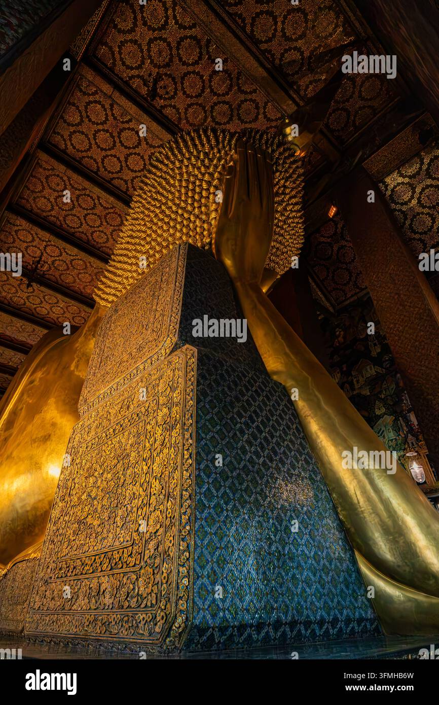 Nahaufnahme des Gesichts der goldenen liegenden Buddha-Statue, eingerahmt zwischen farbenfrohen Mosaiksäulen im Wat Pho Tempel in Bangkok Stockfoto