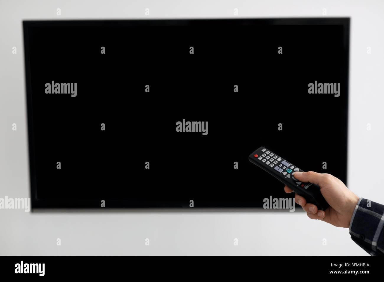 Leere Plasma-Fernbildschirm und männliche Hand mit Fernbedienung, während der Zuschauer Kanäle über eine graue Wand im Innenraum schaltet. Werbe-Mockup. Technik Stockfoto