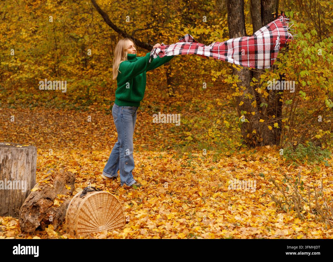 Frau breitet karierte Decke für Picknick im Herbstpark aus Stockfoto