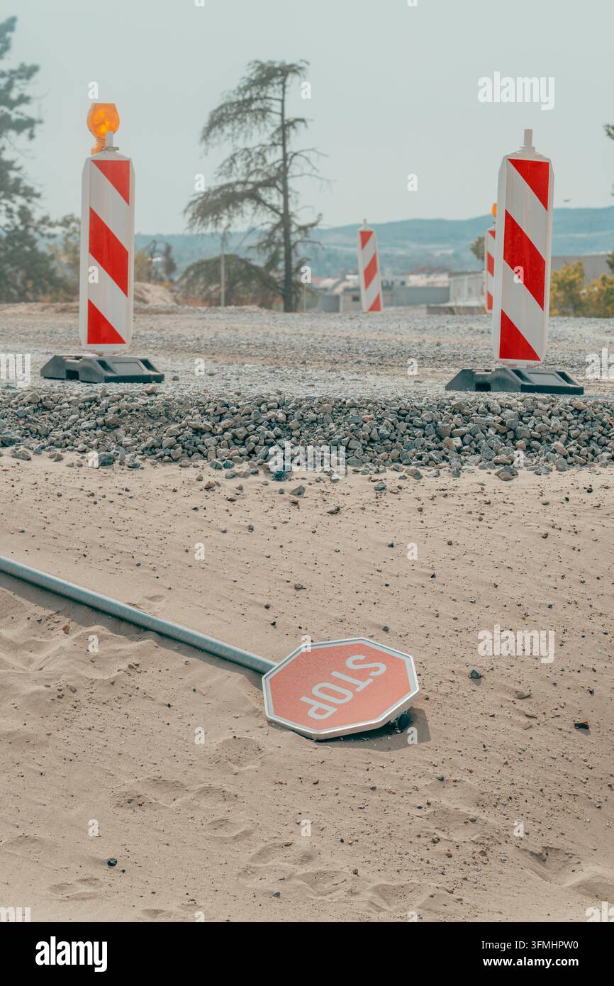 Umgestürztes Stoppschild, das auf Sand in einem Baugebiet für Zivilingenieure ruht. Konzept von Gefahren an Baustellen, unterbrochener Verkehrsfluss, Infrastruktur d Stockfoto
