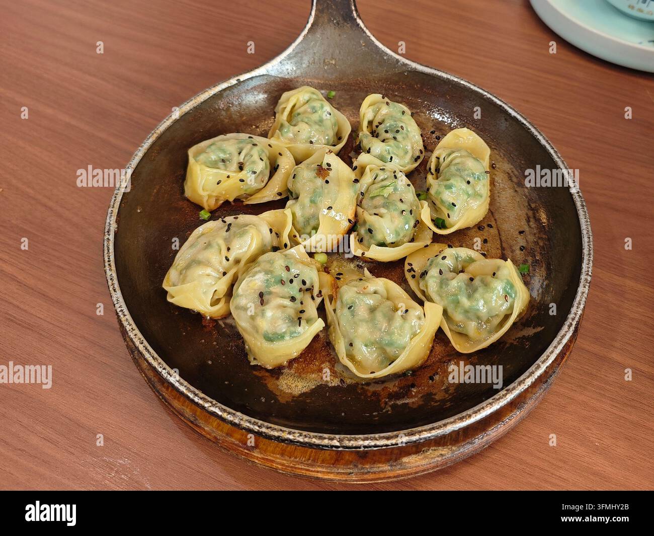 Gebratene Knödel mit schwarzem Sesamsamen und gehackten Frühlingszwiebeln, serviert in einer warmen Gusseisenpfanne Stockfoto