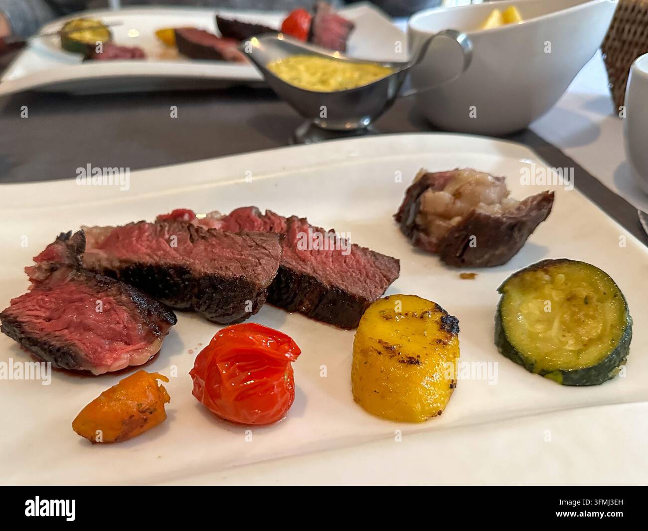 In Scheiben geschnittenes medium rare gegrilltes Steak mit Gemüse auf einem Teller. In Scheiben geschnittenes medium rare gegrilltes Steak auf einem weißen Teller serviert mit geröstetem Gemüse, Kirsch Stockfoto