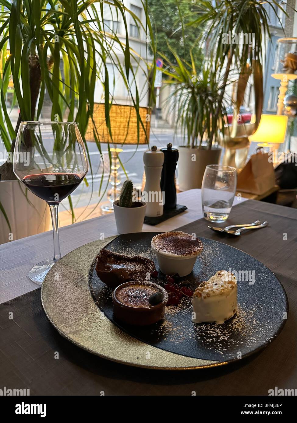 Verschiedene Gourmet-Desserts auf einem stilvollen Teller neben einem Glas Rotwein in einer Restaurant-Atmosphäre Stockfoto