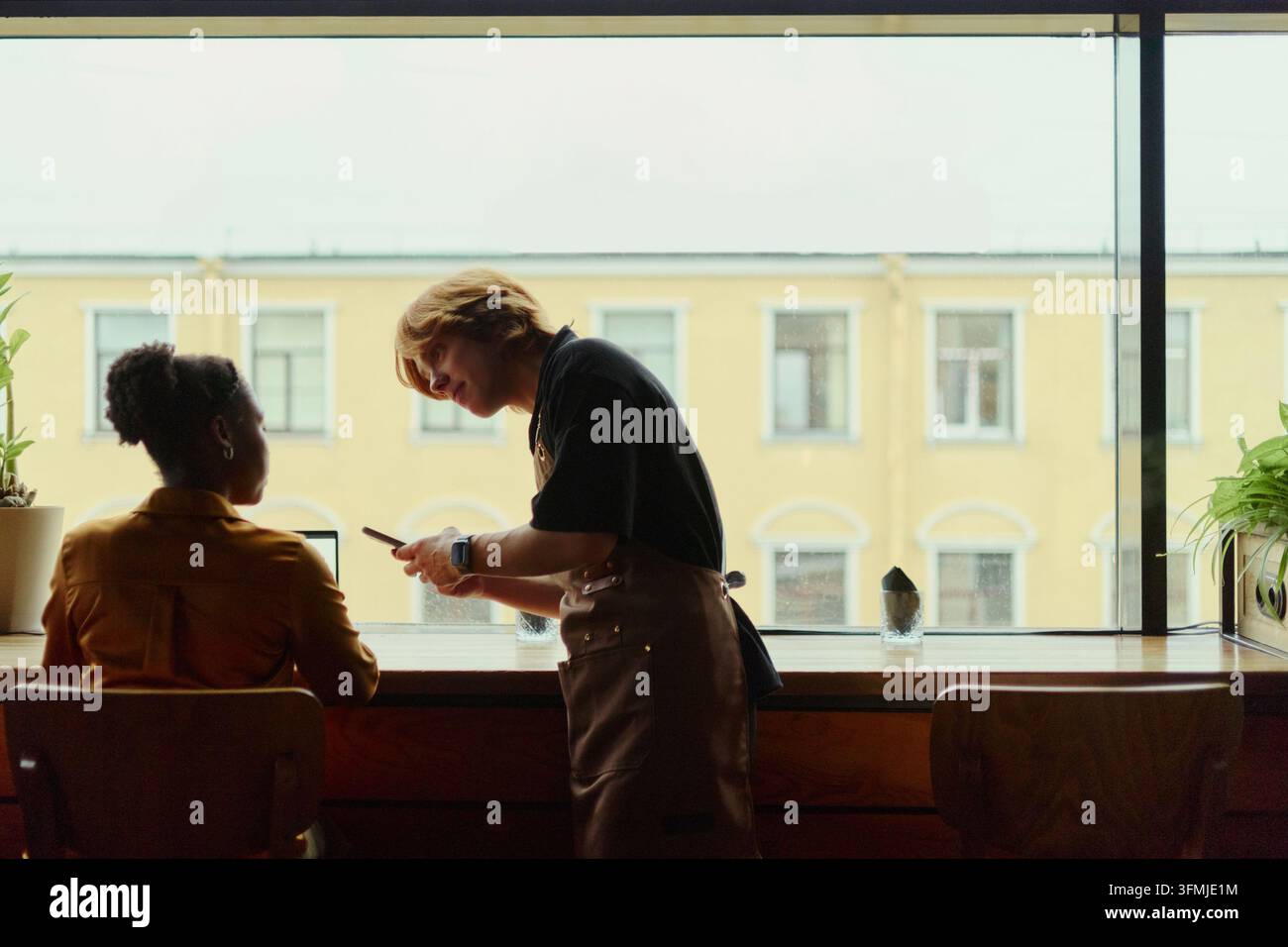 Barista nimmt Bestellung von schwarzer Frau mit Smartphone im Café auf Stockfoto