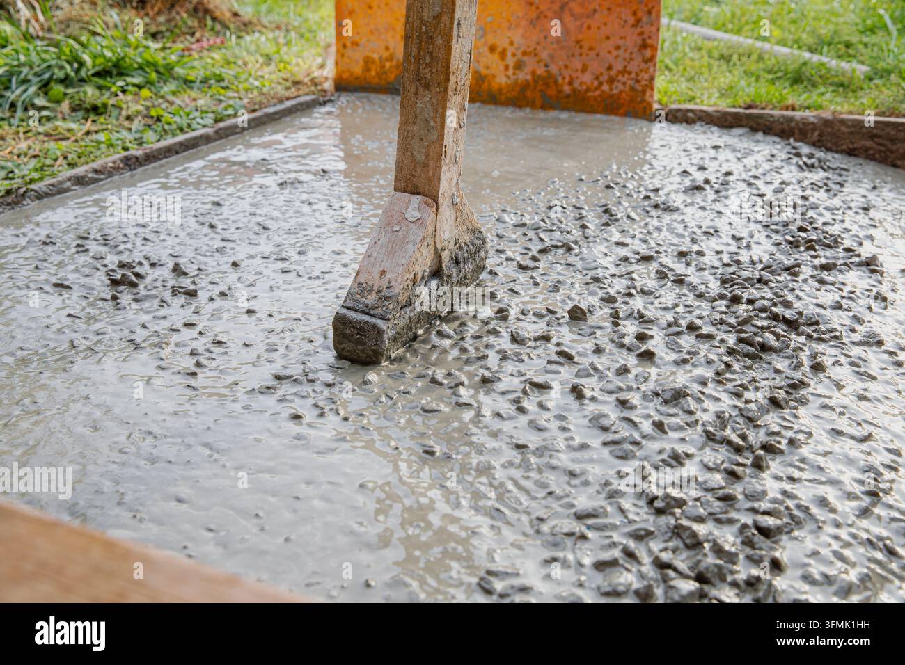 Holzhandschneidewerk glättet frischen Beton, der mit Kies auf einem Weg vermischt ist Stockfoto