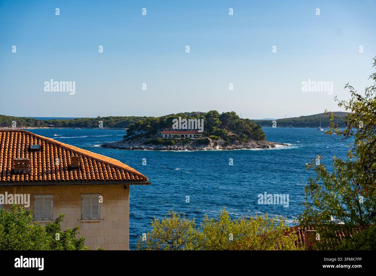 Panoramablick von der Stadt Hvar auf eine Küsteninsel mit einem Haus, umgeben von türkisblauem Wasser und einem klaren blauen Himmel in Kroatien Stockfoto