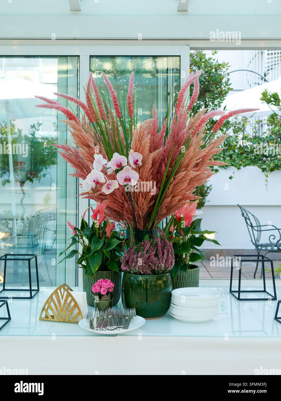 Dekoratives Blumenarrangement mit rosa Orchideen und Gräsern in grünen Vasen auf einem Tisch im Freien. Stockfoto