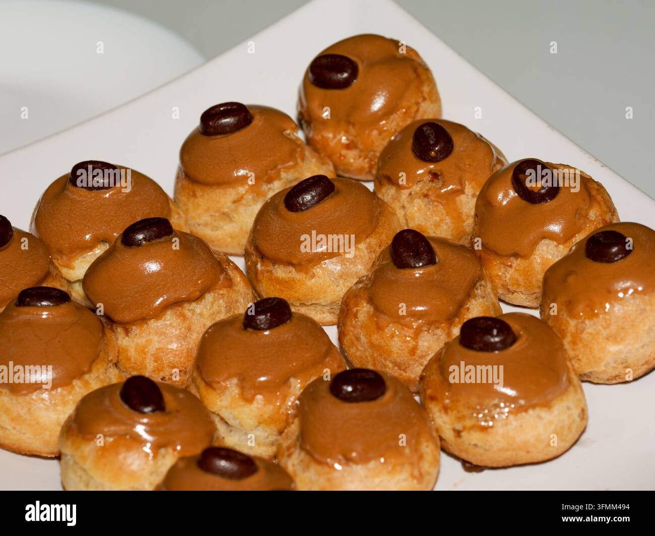 Teller mit Kaffeekrapfen, die mit Kaffeebohnen auf weißem Hintergrund belegt sind. Stockfoto