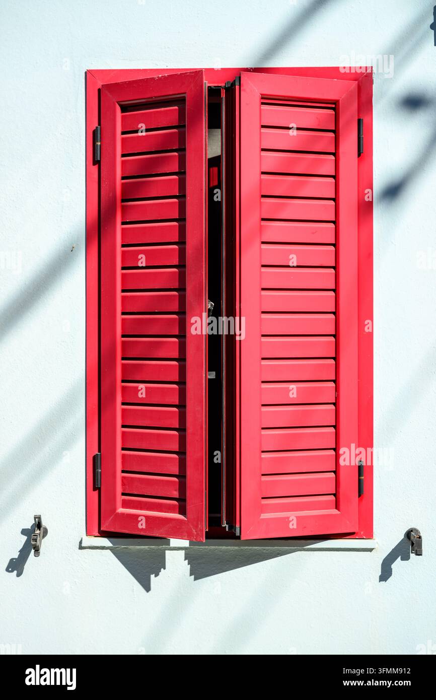 Rote offene Fensterläden an einer weißen Wand Stockfoto