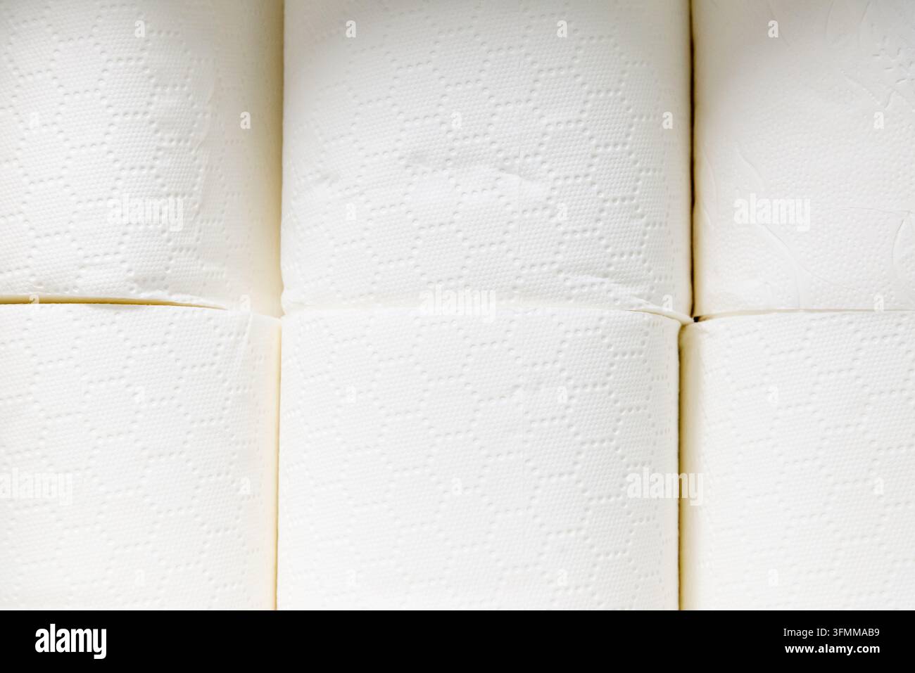 Nahaufnahme von gestapelten weißen Toilettenpapierrollen mit geprägtem Muster. Stockfoto