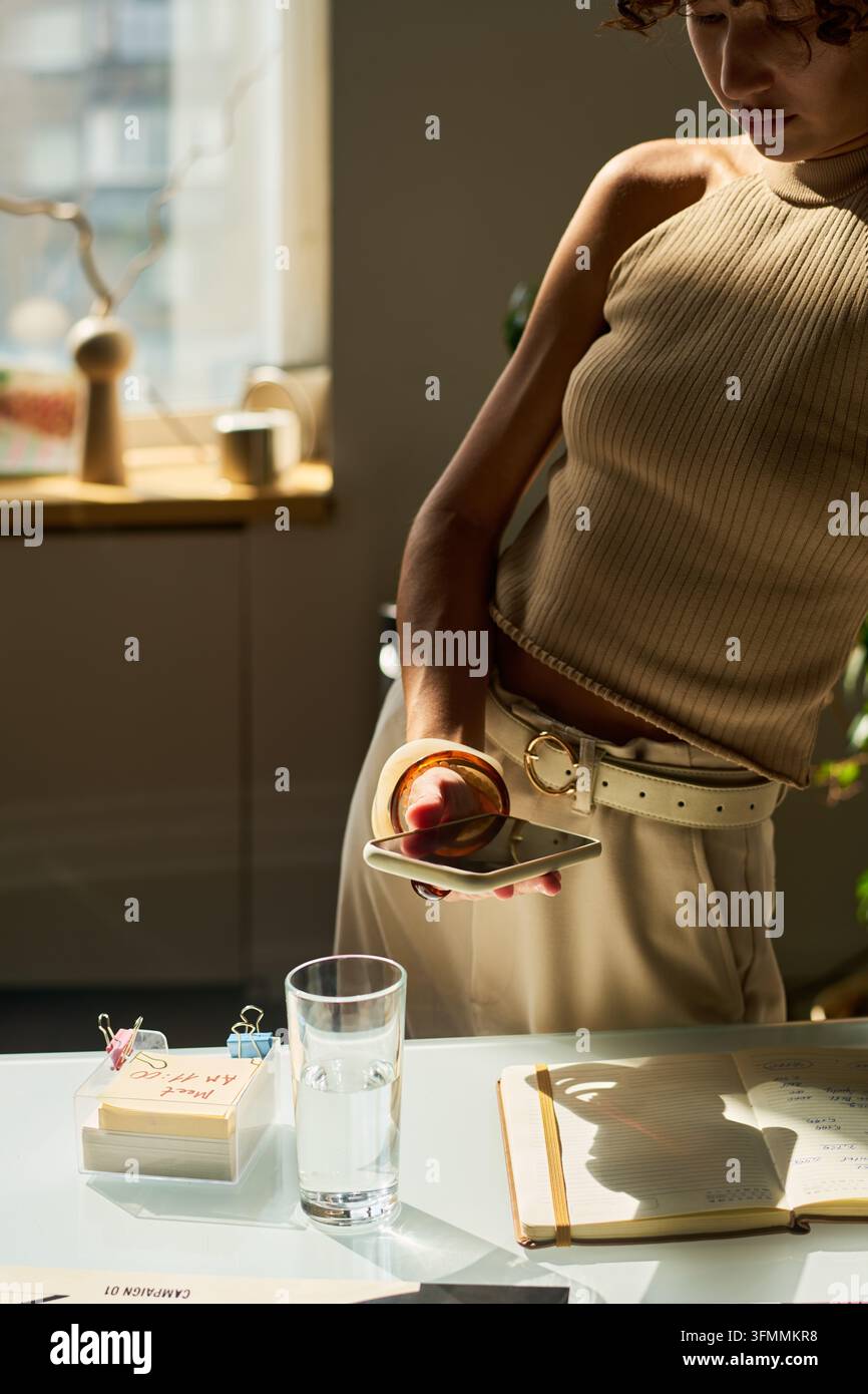 Bikulturelle Designerin überprüft Smartphone am kreativen Bürotisch Stockfoto