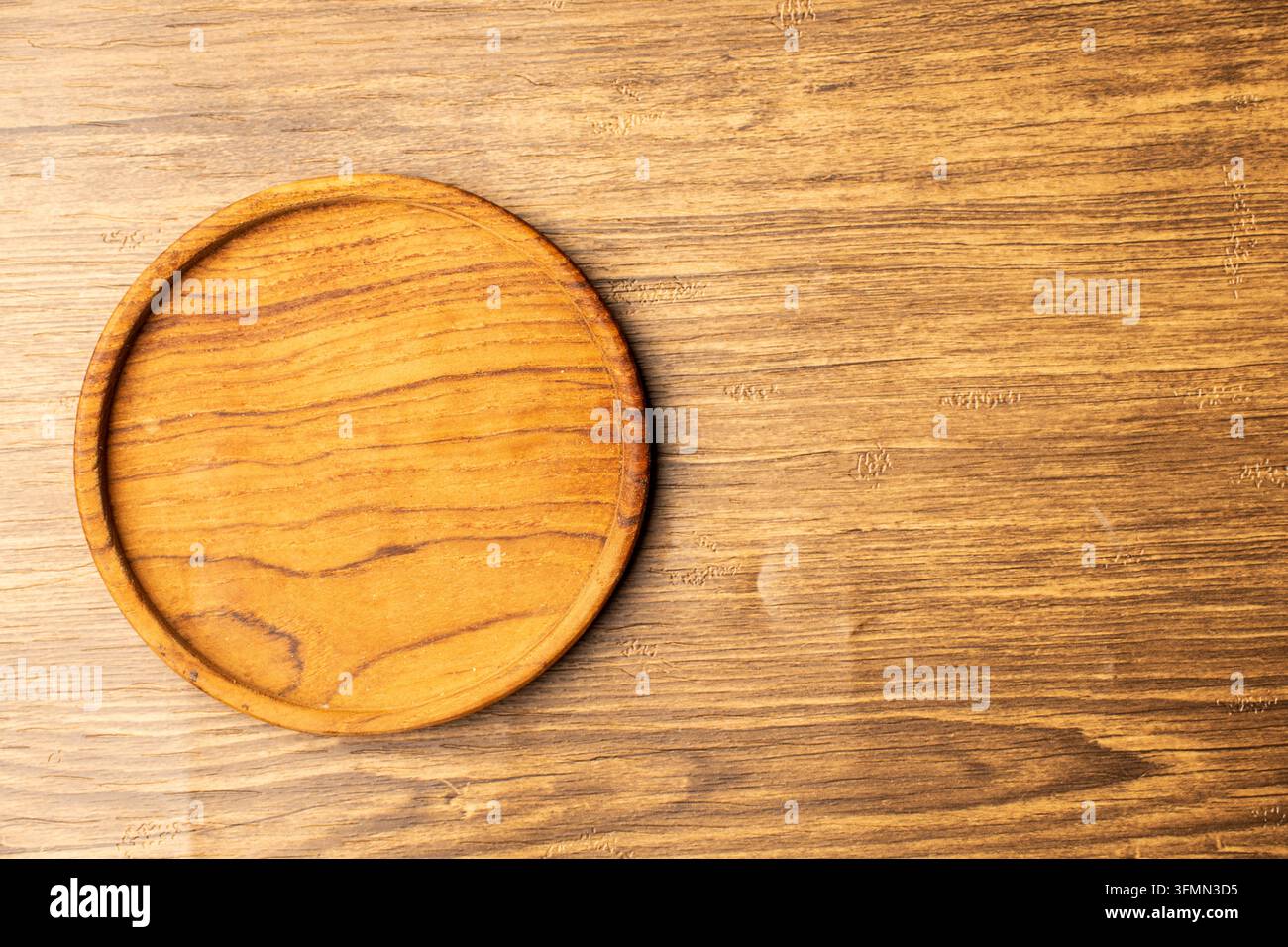 Flache Lage, Top-Down-Ansicht eines leeren runden Holzuntersetzers, der auf rustikalem Holzgrund platziert ist, mit warmer Beleuchtung und breitem Kopierraum rechts. Stockfoto