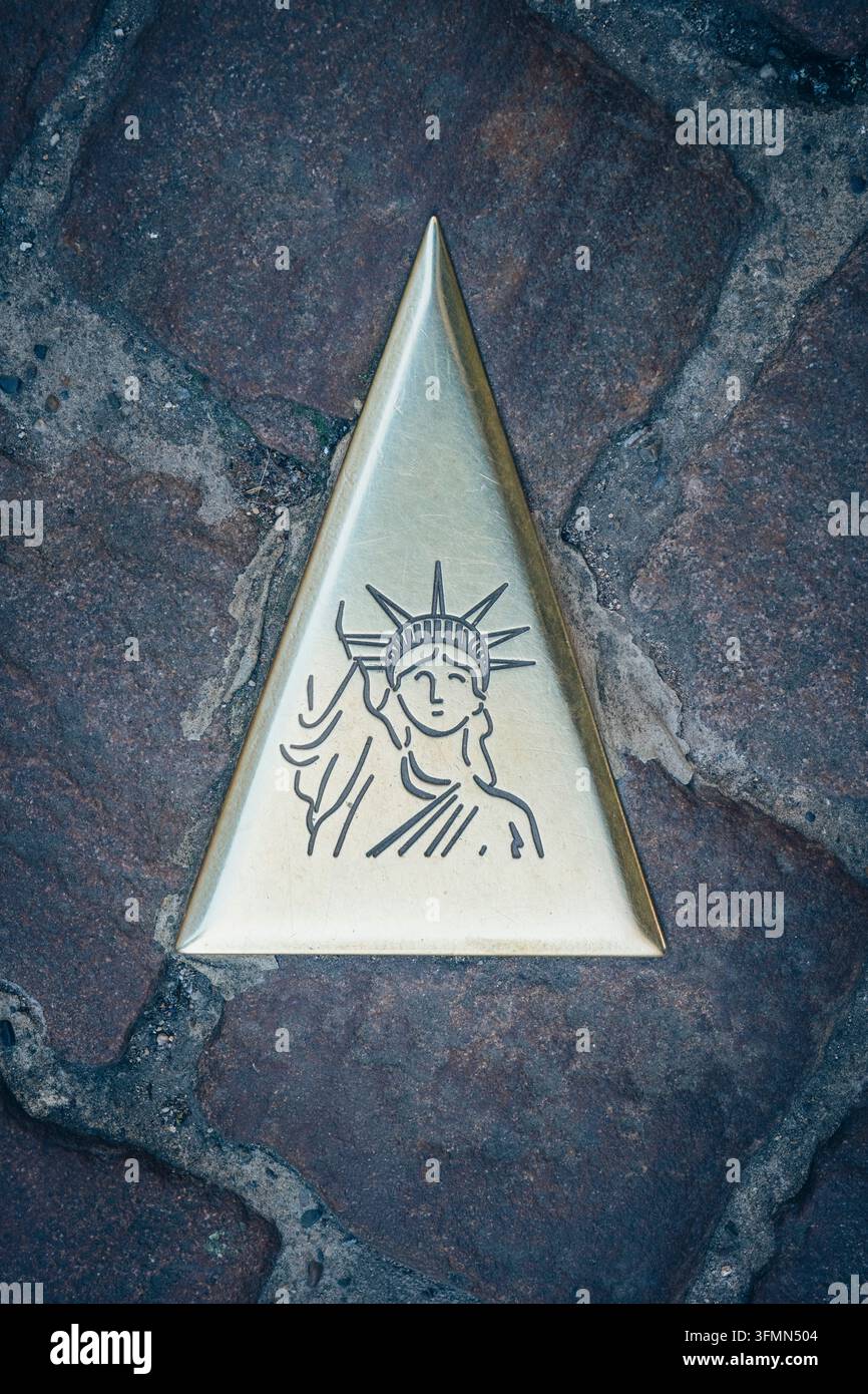 Nahaufnahme einer dreieckigen Metallplakette mit der Silhouette der Freiheitsstatue als Touristenführer im grauen Steinboden, im historischen alten Kai Stockfoto