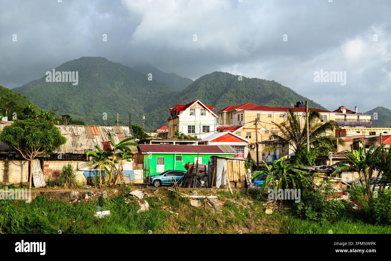 Prachtvolle Aussicht auf farbenfrohe Häuser und üppige grüne Berge unter einem bewölkten Himmel in Roseau, Dominica. Stockfoto