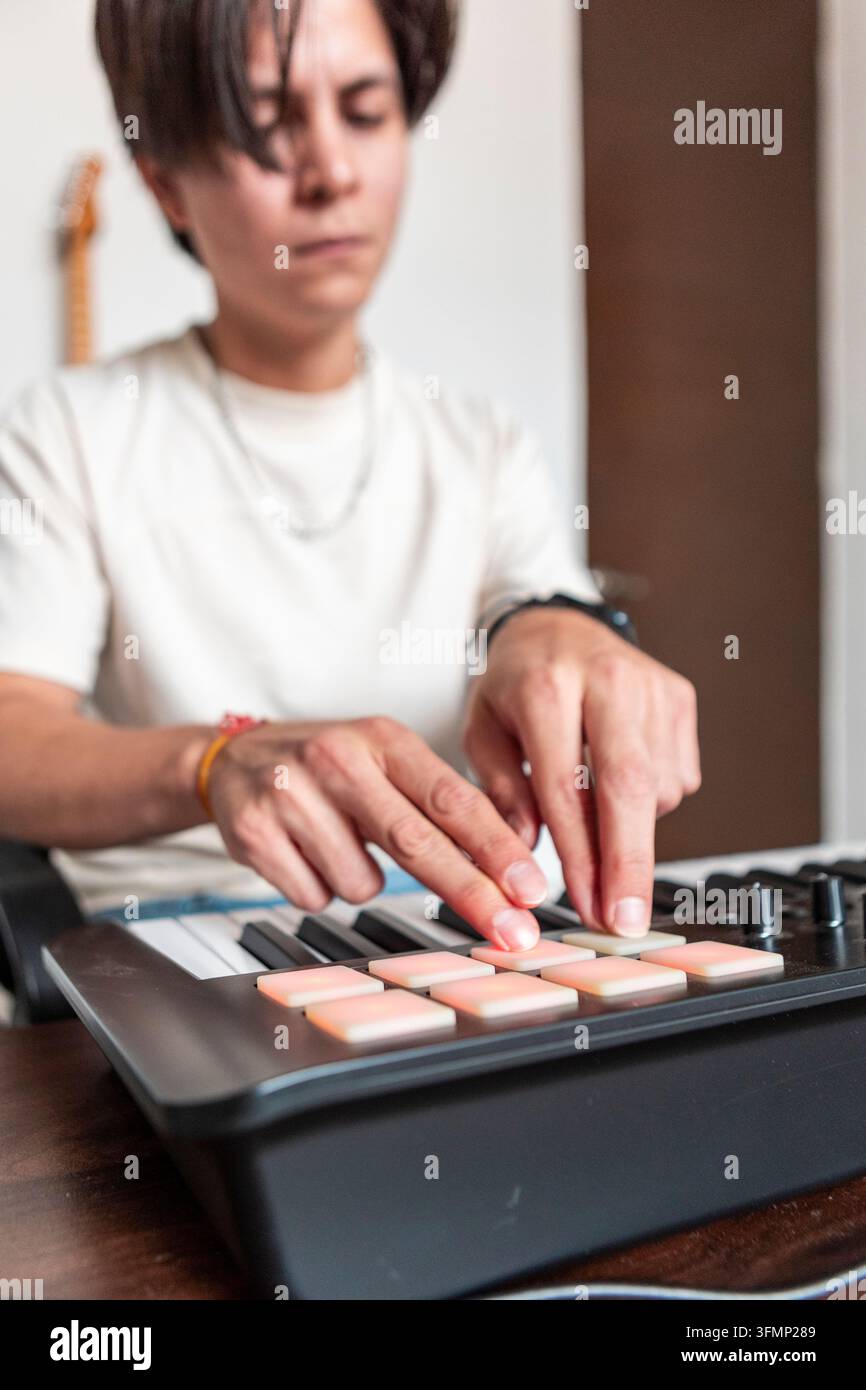 Junger Musikkomponist erstellt elektronische Beats auf einem Pad-Controller zu Hause, wobei er konzentrierte Hände verwendet, um beleuchtete Tasten neben einem Keyboard auszulösen. Stockfoto