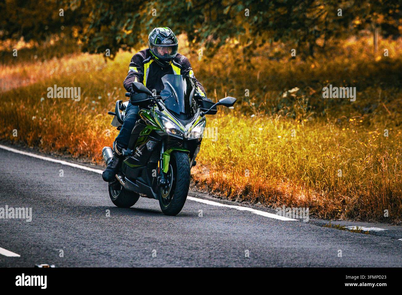 Ein Motorradfahrer fährt ein grün-schwarzes Kawasaki-Sportmotorrad entlang einer Landstraße im Herbst Stockfoto