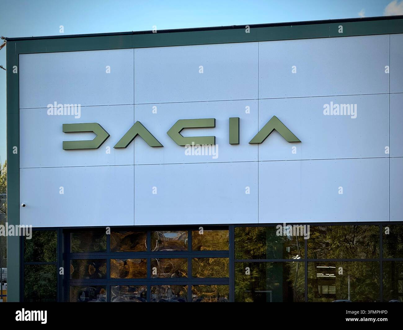 Geradaufnahme der Fassade eines offiziellen Dacia-Autohandels mit dem neuen geometrischen Dacia-Schriftzug auf weißen Paneelen über dem gläsernen Ausstellungsraum - Smartphone-aufgenommenes Stockfoto