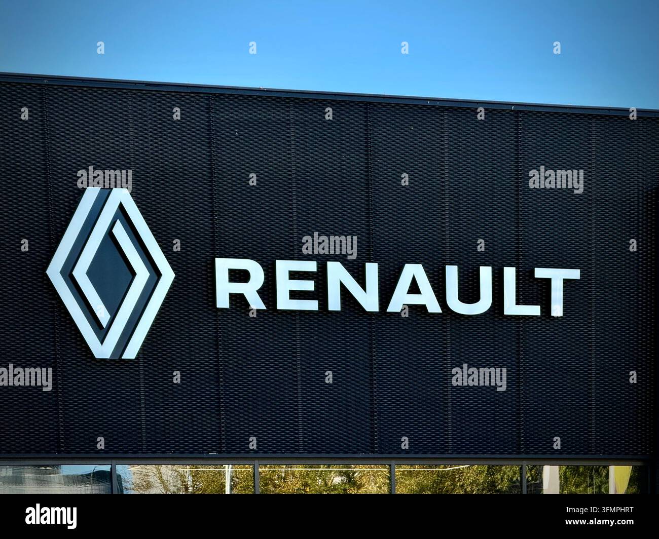 Außenaufnahme eines offiziellen Renault-Autohandels mit einem weißen geometrischen Diamantlogo und Wortmarke auf einer dunklen Netzfassade unter einem klaren blauen Himmel - Smartphone-aufgenommenes Stockfoto