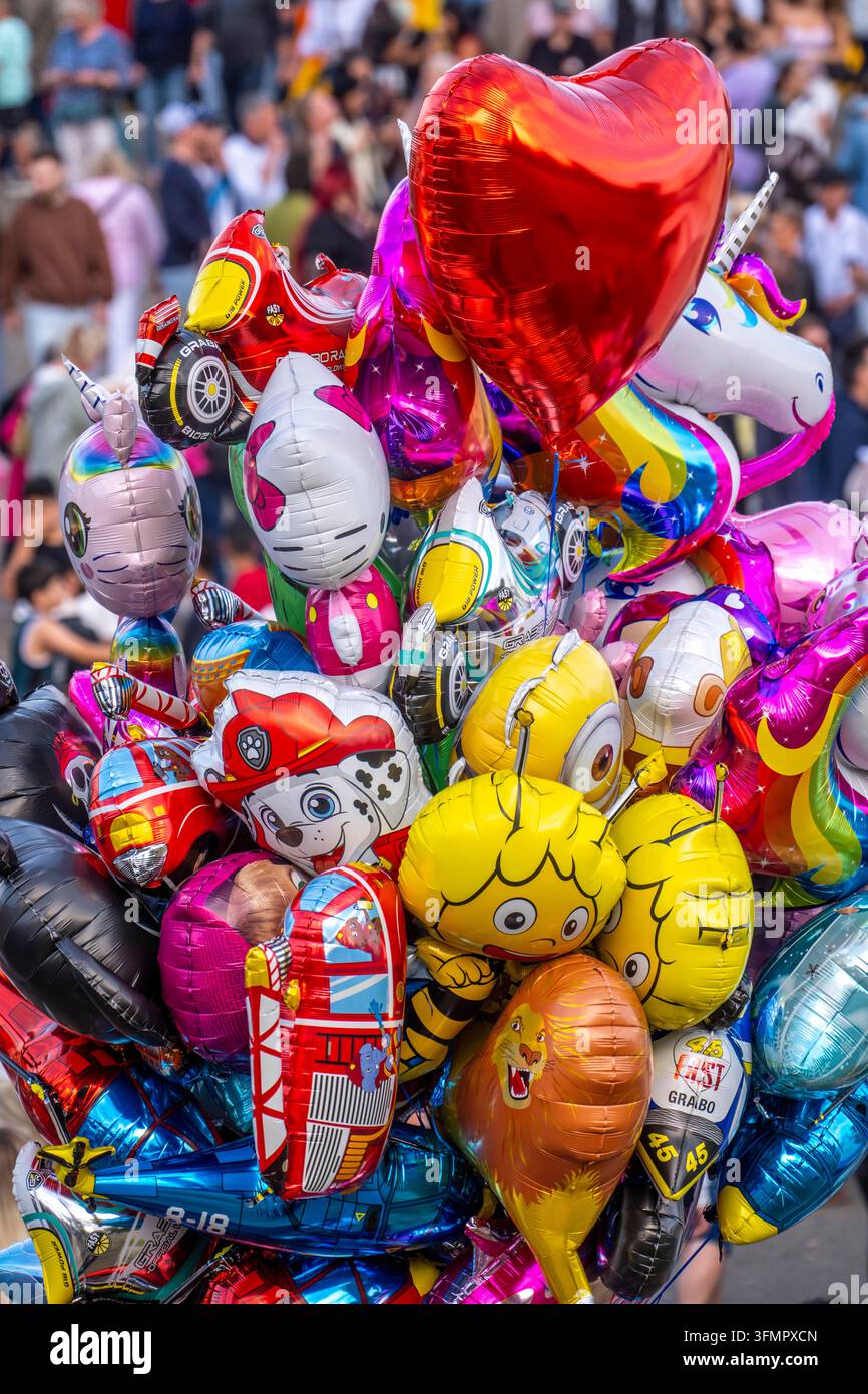 Viele bunte Themenballons, mit Gas gefüllt, schweben in der Luft und zeigen viele verschiedene Designs, darunter Cartoonfiguren und Symbole Stockfoto