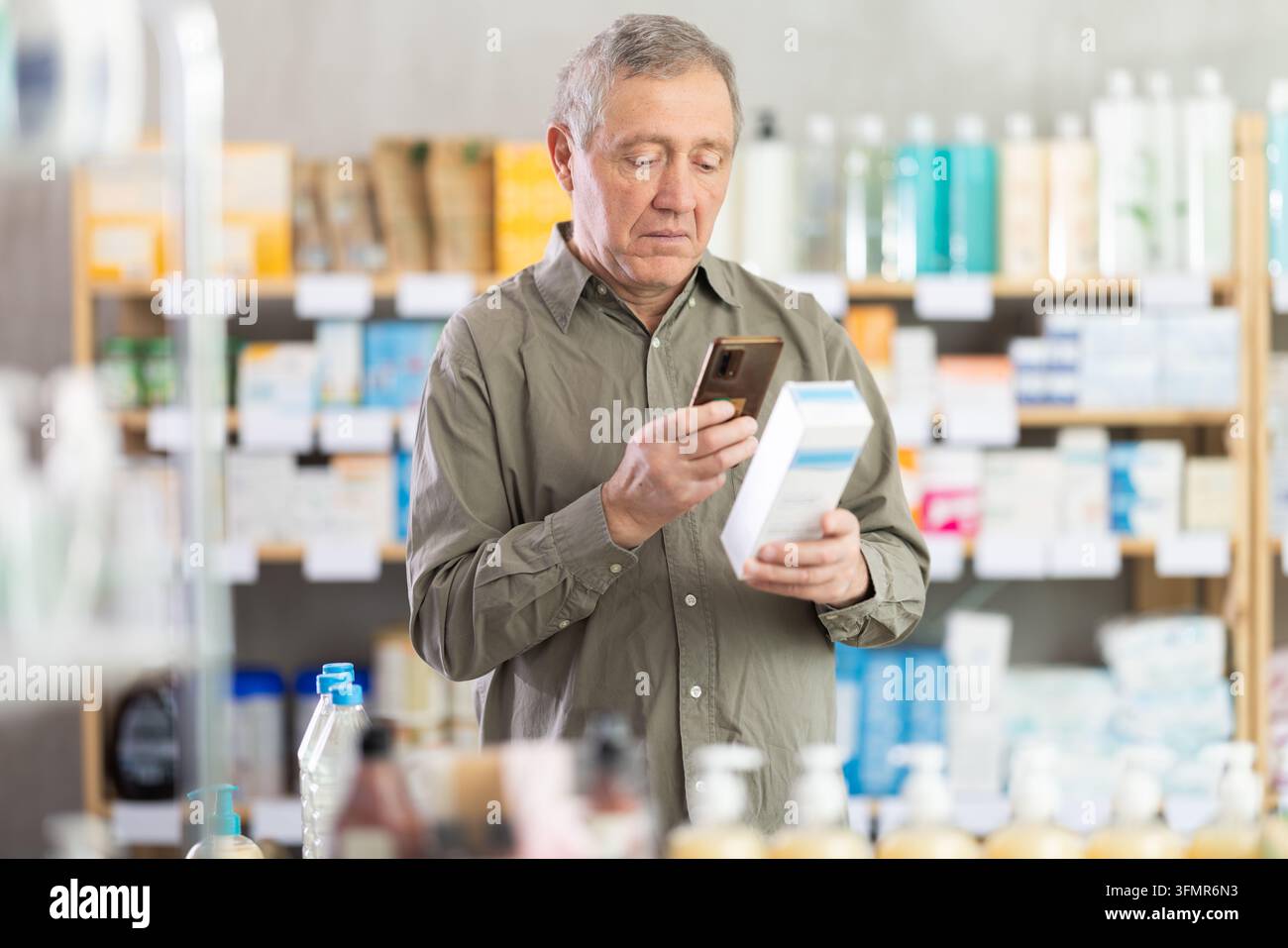 Senior Mann in der Apotheke scannt den QR-Code auf einer Atopik-Creme und nutzt den Link, um zur Website des Herstellers zu gelangen. Stockfoto