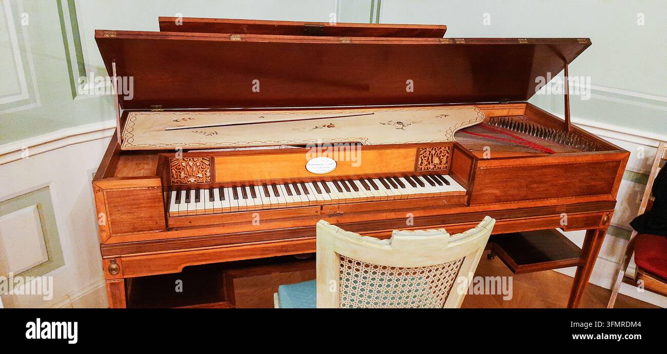 Antikes hölzernes Clavichord-Tastaturinstrument mit geöffnetem Deckel und einem Rohrsessel davor - Warschau, Polen - 26. Januar 2023 Stockfoto