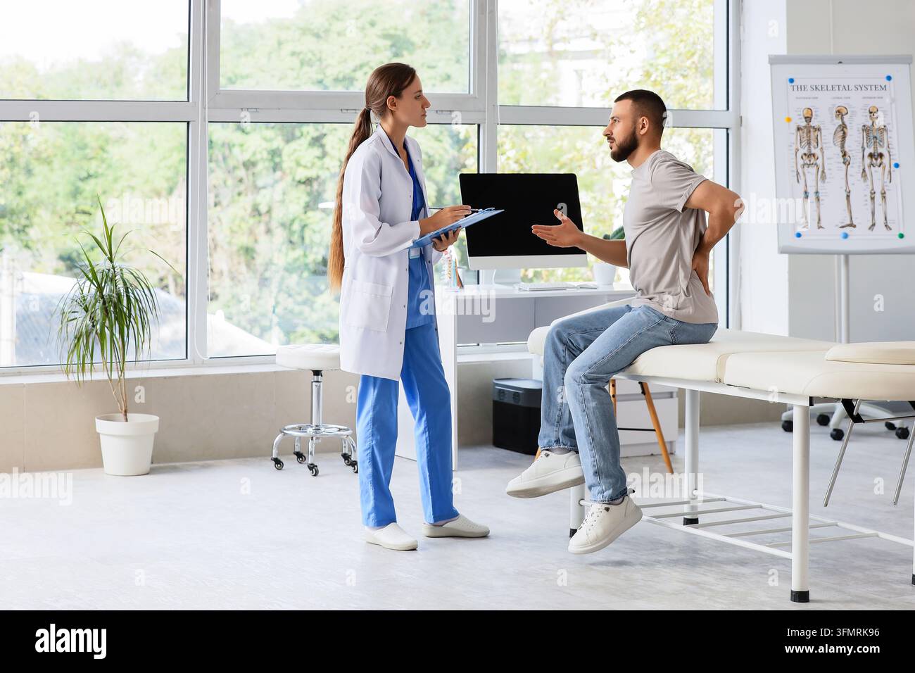 Rückenschmerz-Konsultation, Arzt untersucht männlichen Patienten mit Wirbelsäulenverletzung oder chronischen Beschwerden in einem modernen medizinischen Klinikbüro mit Skelettsystem Stockfoto