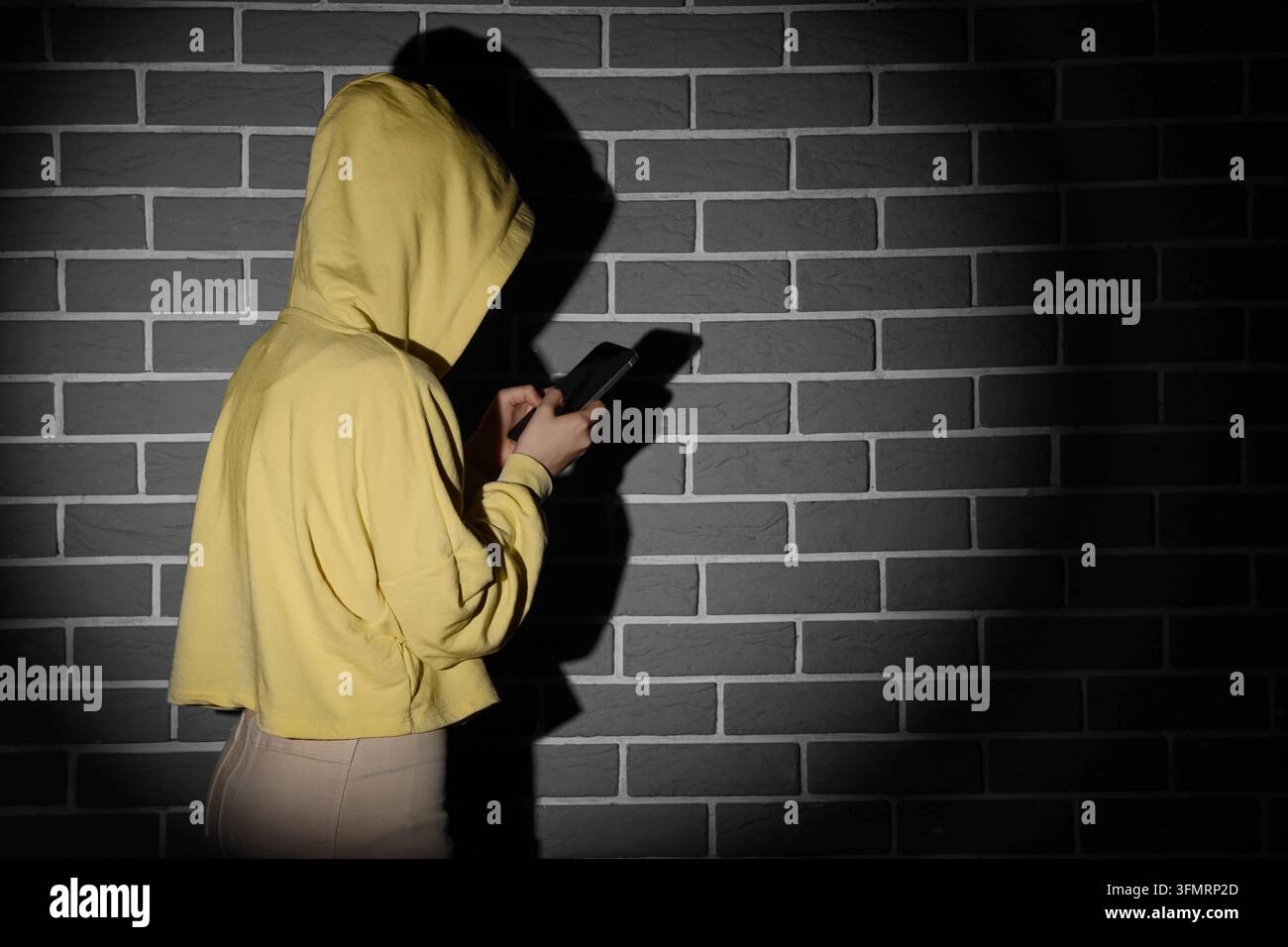 Cybermobbing und Social-Media-Sucht, anonyme Person in einem Hoodie, die ein Smartphone verwendet, mit dunklem Schatten an einer Ziegelwand online Belästigung Stockfoto