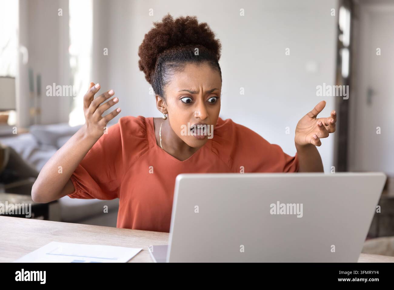 Frau hebt ungläubig die Hände und starrt auf den Laptop-Bildschirm Stockfoto