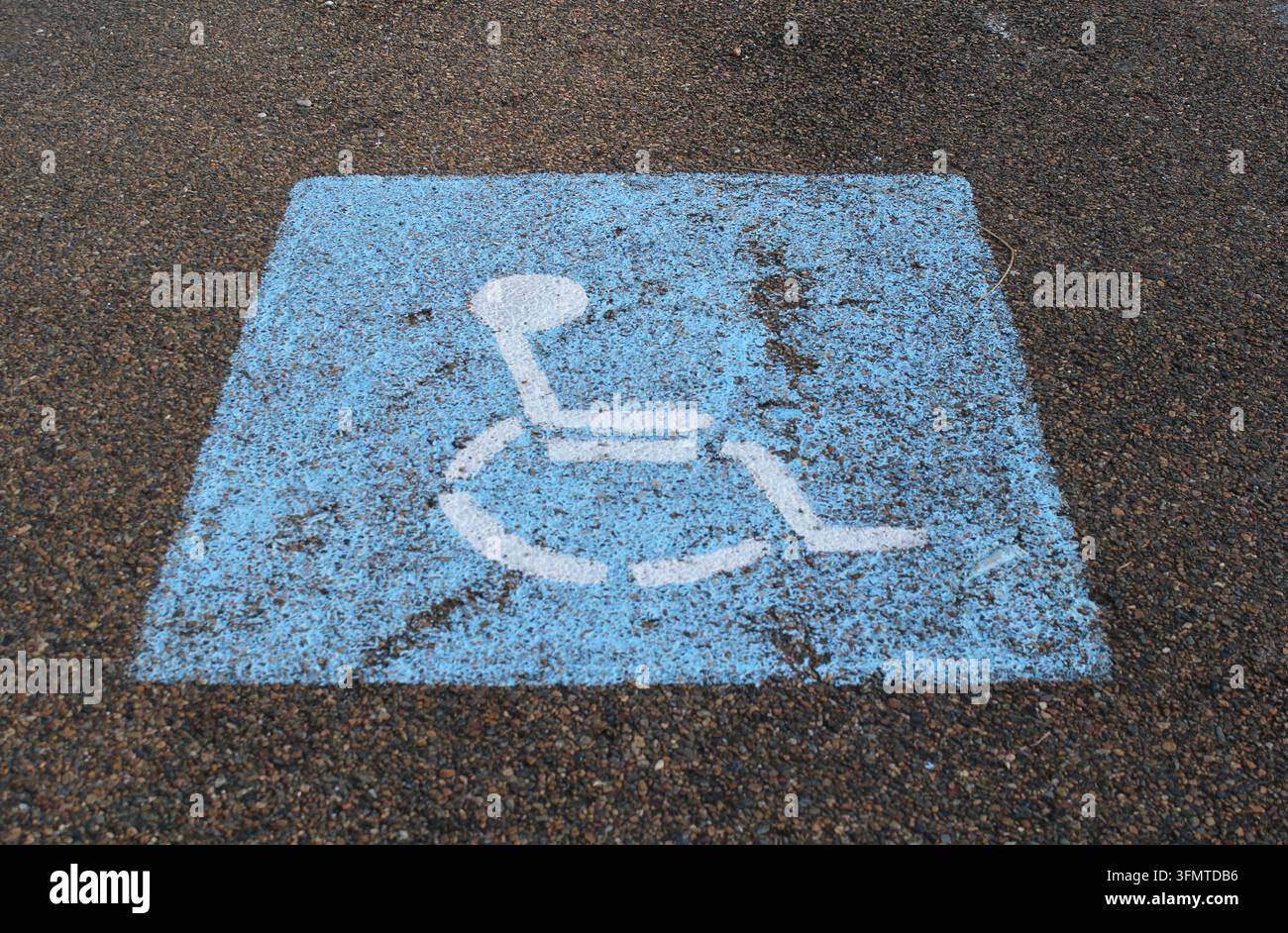 Hochwinkelansicht eines verwitterten blauen und weißen Behindertenparkplatz-Symbols, das auf einen Asphaltparkplatz gemalt ist Stockfoto